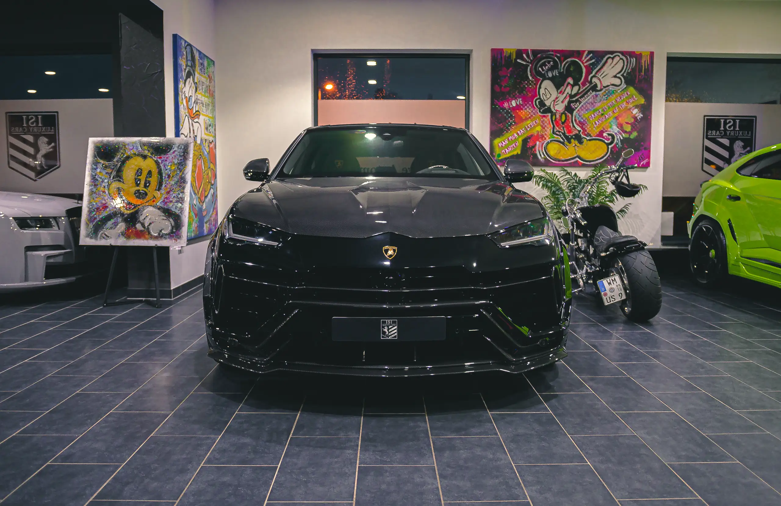 Schwarzer Lamborghini Urus von vorne, an den Wänden Pop-Art-Bilder