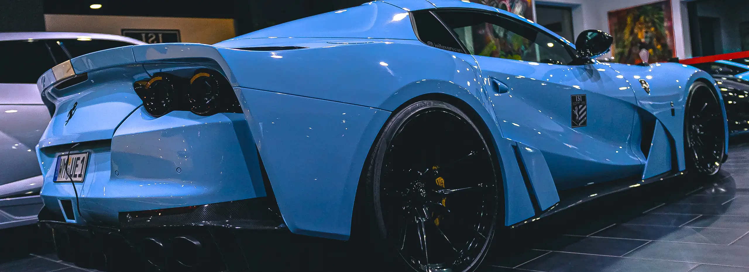 Heckansicht eines hellblauen Ferrari mit Kennzeichenhalter von Autohaus ISI
