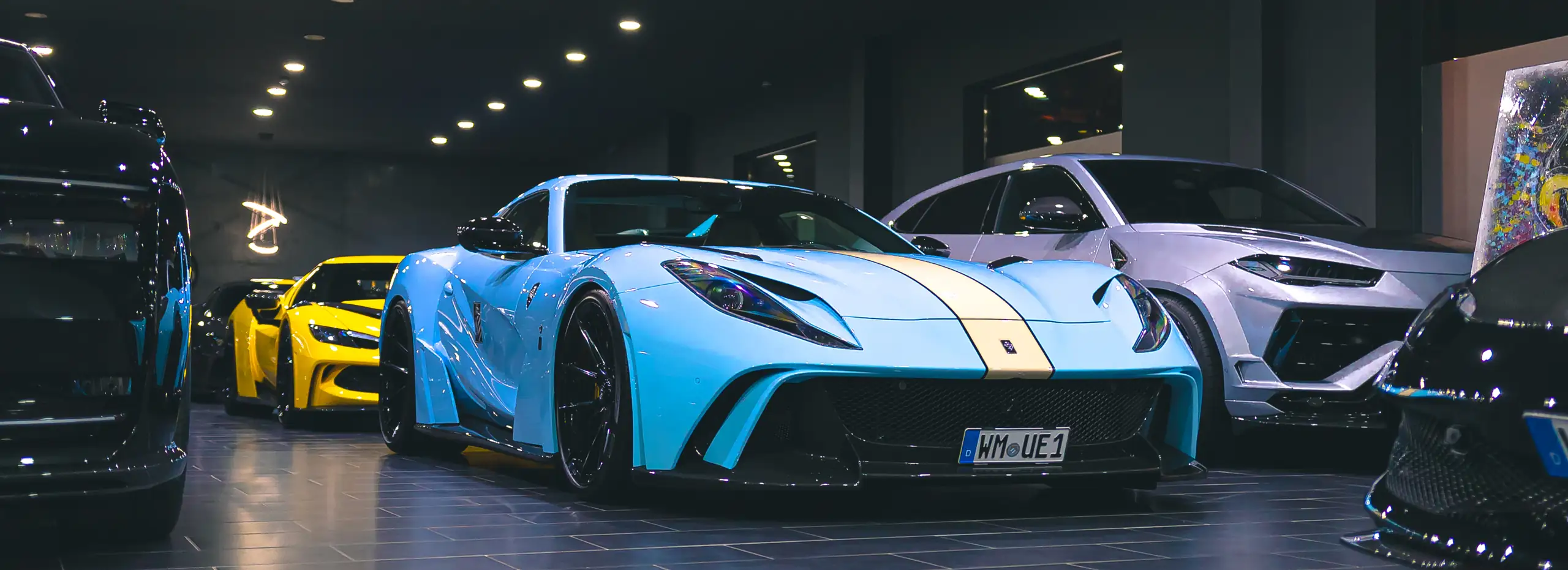 Hellblauer Ferrari im Vordergrund, dahinter die Fahrzeugreihe in der Halle