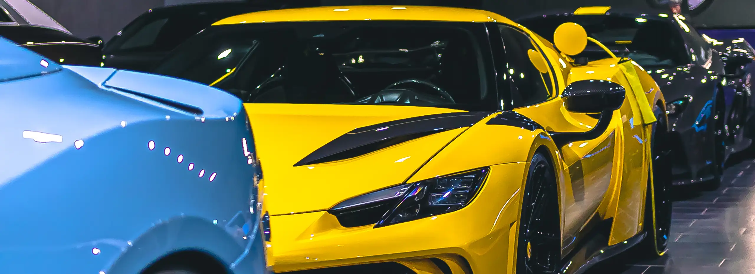 Hellblauer und gelber Ferrari nebeneinander, dahinter ein silberner Lamborghini Urus
