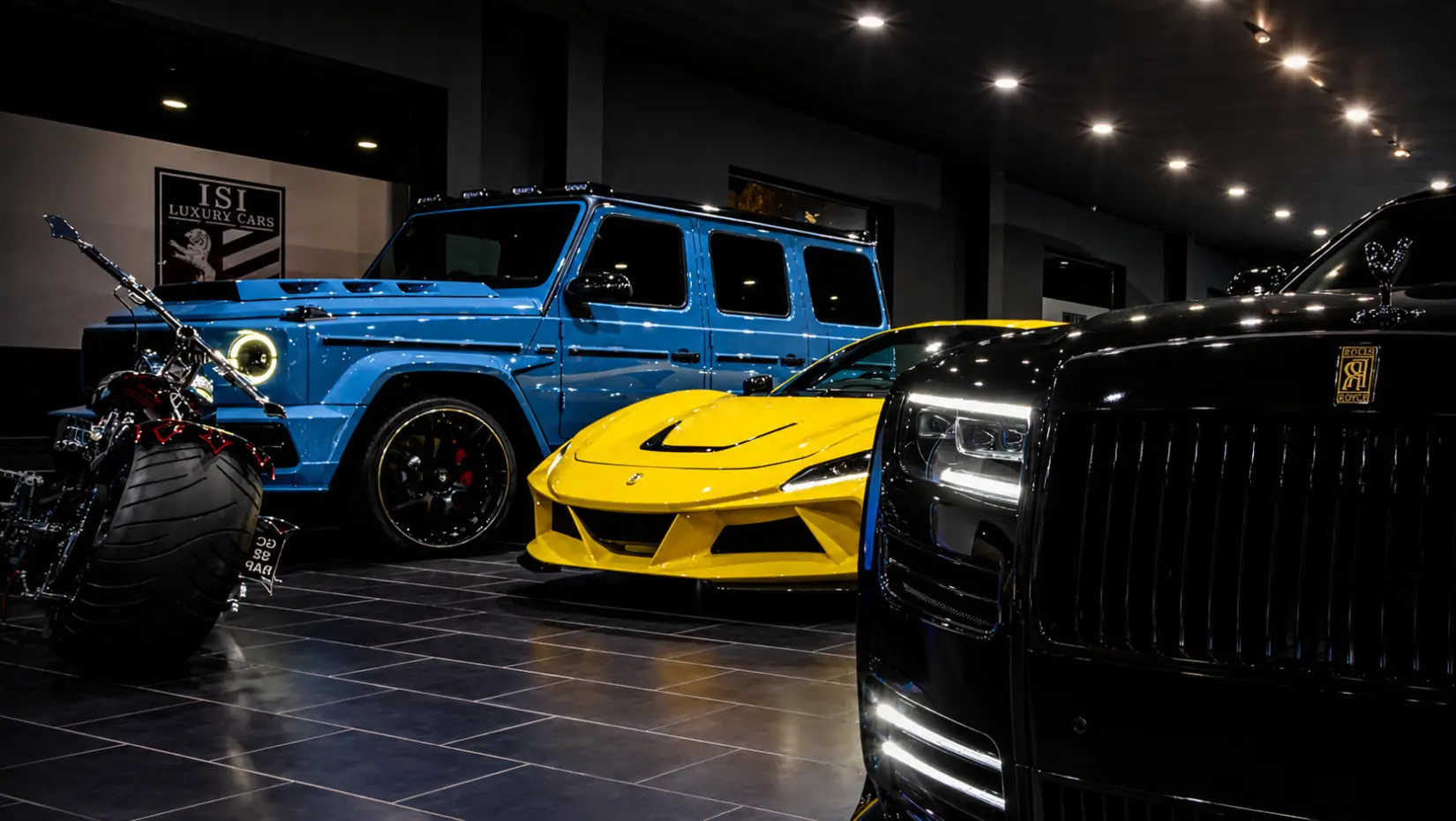 Blauer Mercedes G 63, gelber Ferrari und schwarzer Rolls-Royce im Showroom von Autohaus ISI